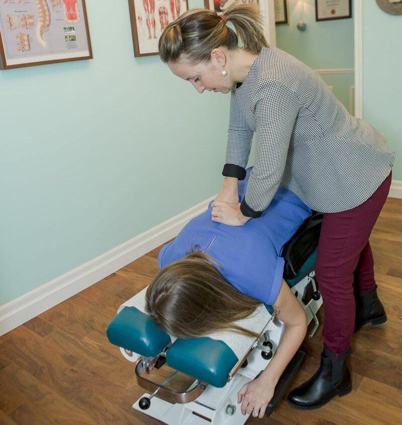 Dr. Maja Edgar working on a client back, while client is laying face down on a chiropractic table.