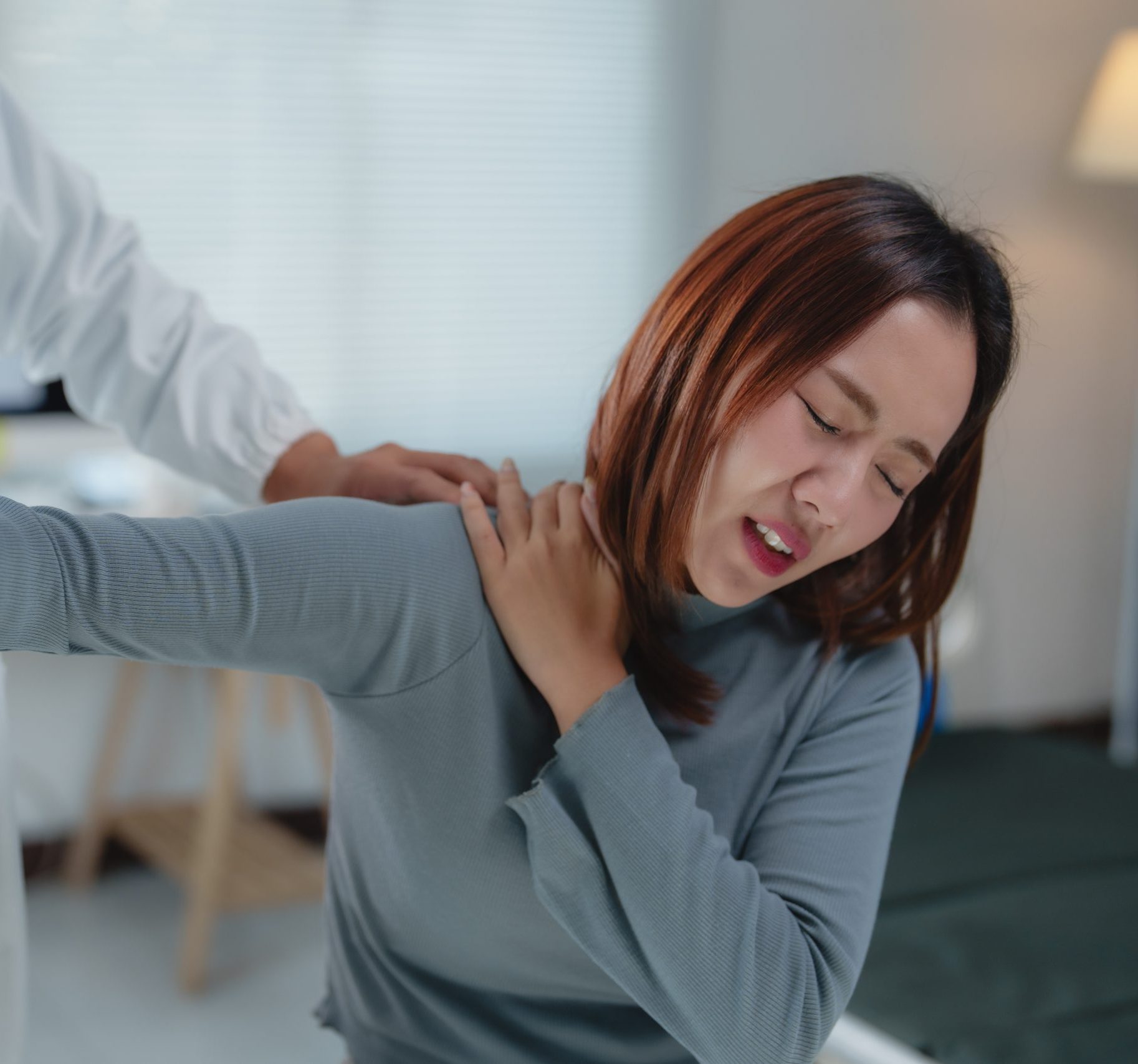 A woman sitting down indicating to a doctor behind her where the neck or shoulder pain is.