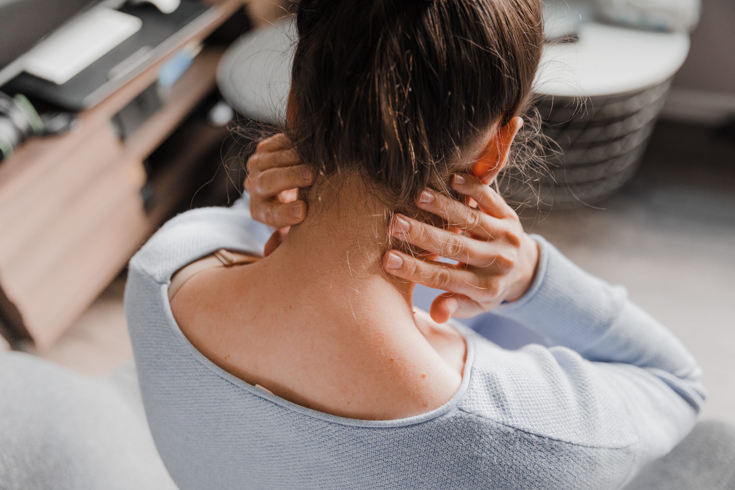 A woman sitting down on a bed holding her neck, in pain or discomfort.