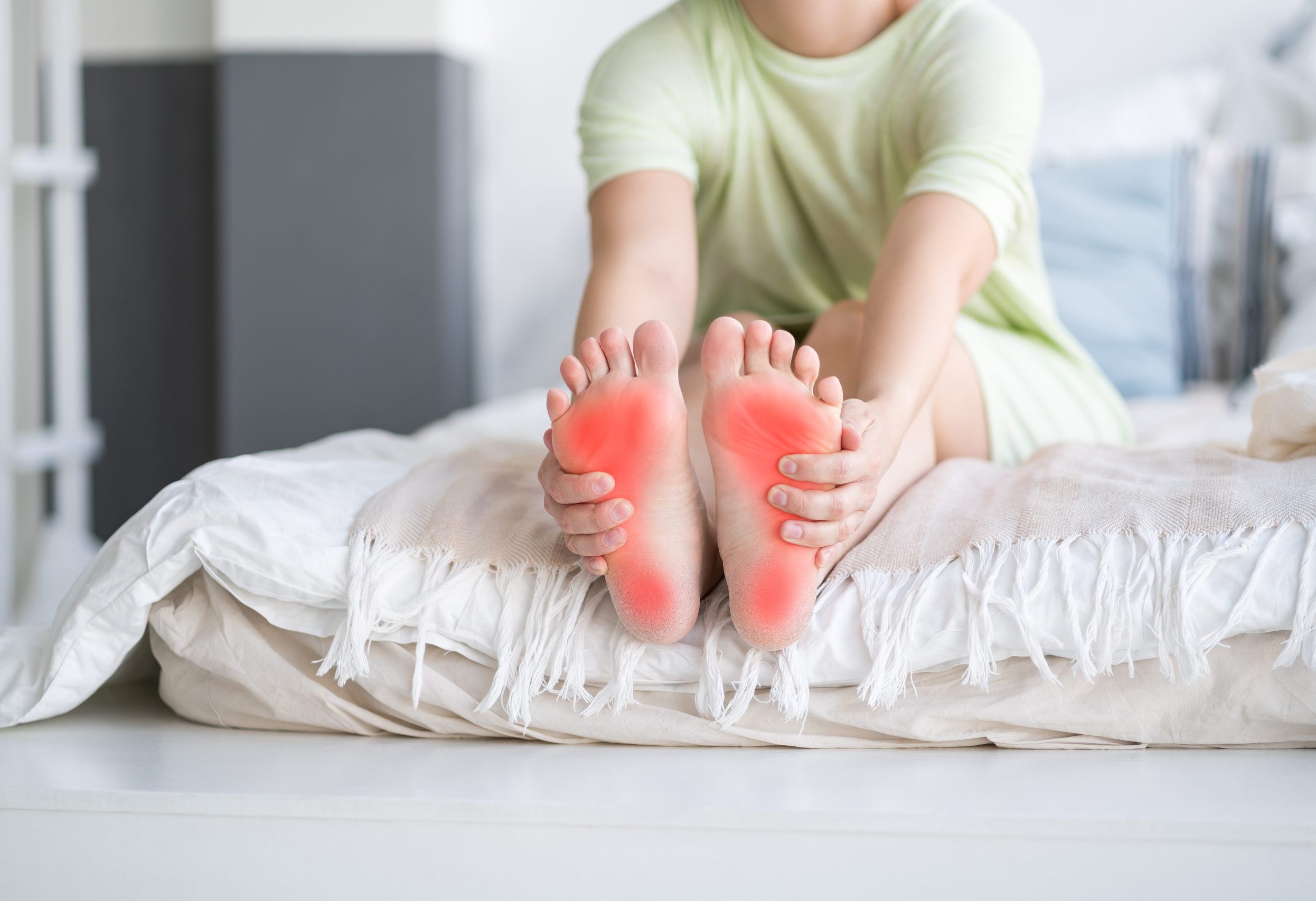A woman sitting on her bed holding her feet with red indicating pain or discomfort.