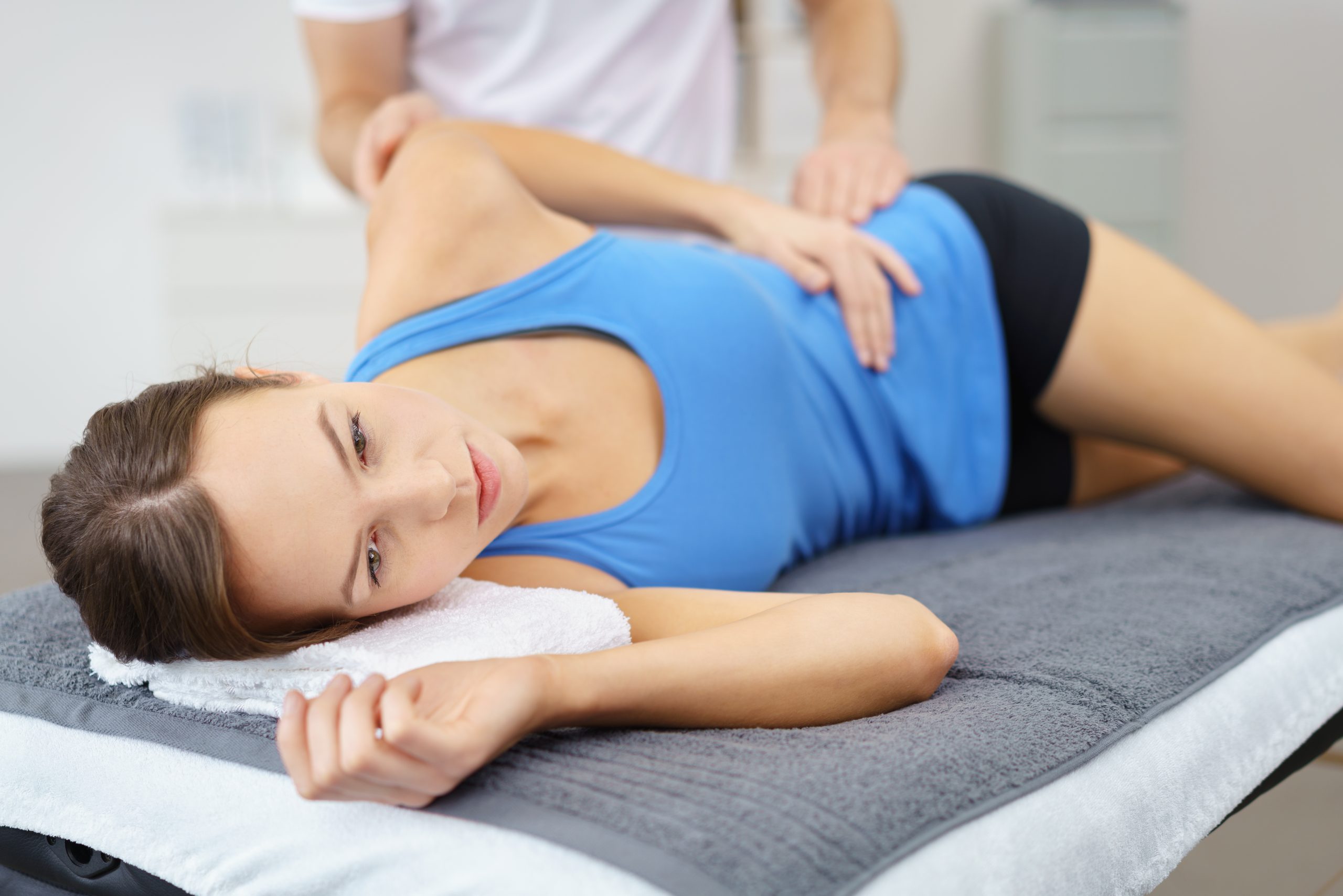 A woman laying on her side, while a doctor is helping with exercises.