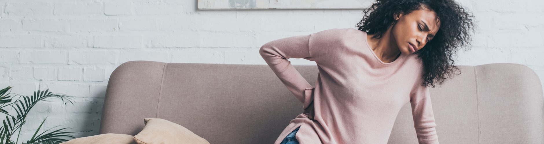 A female sitting down holding her lower back in discomfort.