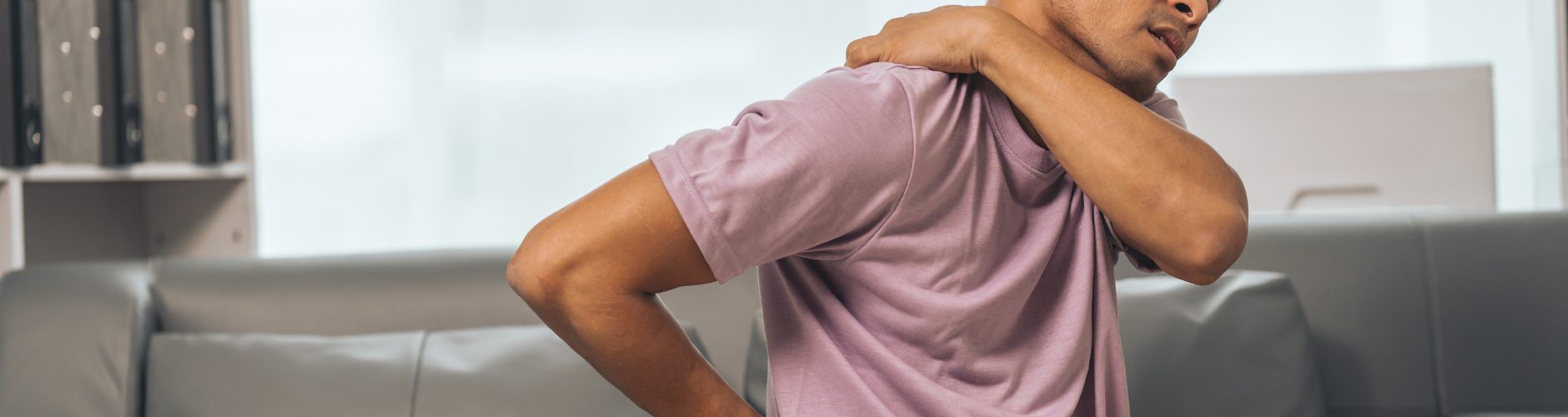 A man sitting down holding his lower back and upper back in discomfort/pain.