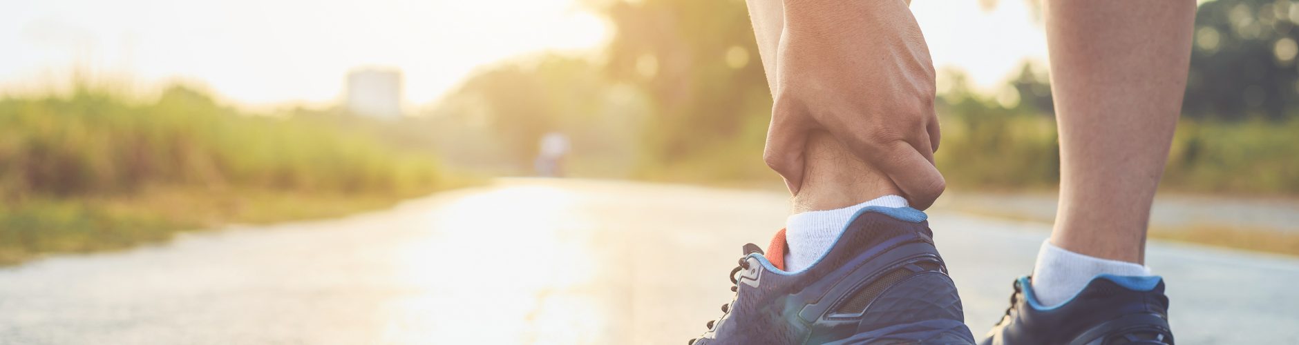 A man holding his left ankle in pain or discomfort while outside.