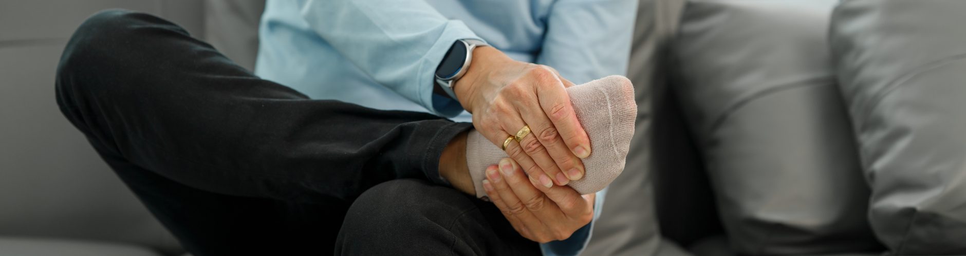 A man sitting down feeling his right foot in pain or discomfort.