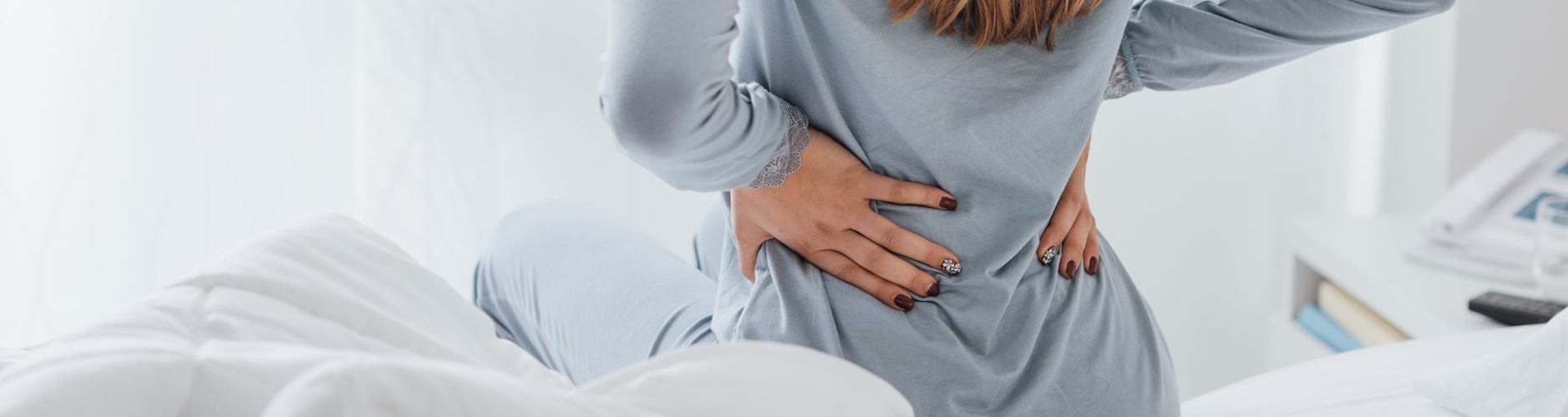 A female sitting over holding her lower back in discomfort.