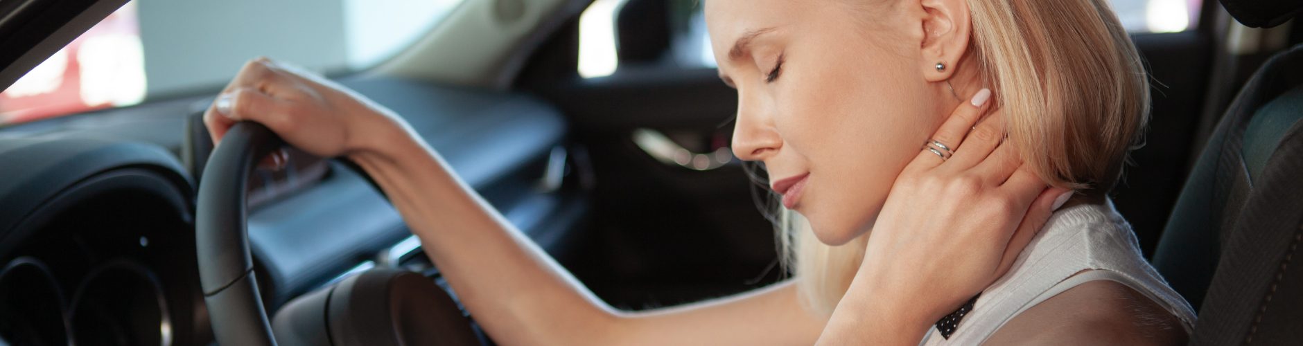 A woman holding neck, appearing in pain or discomfort in a car.