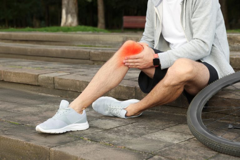Cyclist sitting on stone steps holding a painful knee beside a bicycle after a ride